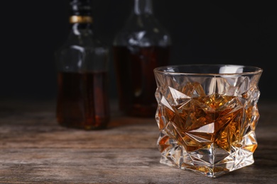 Photo of Golden whiskey in glass with ice cubes on table. Space for text