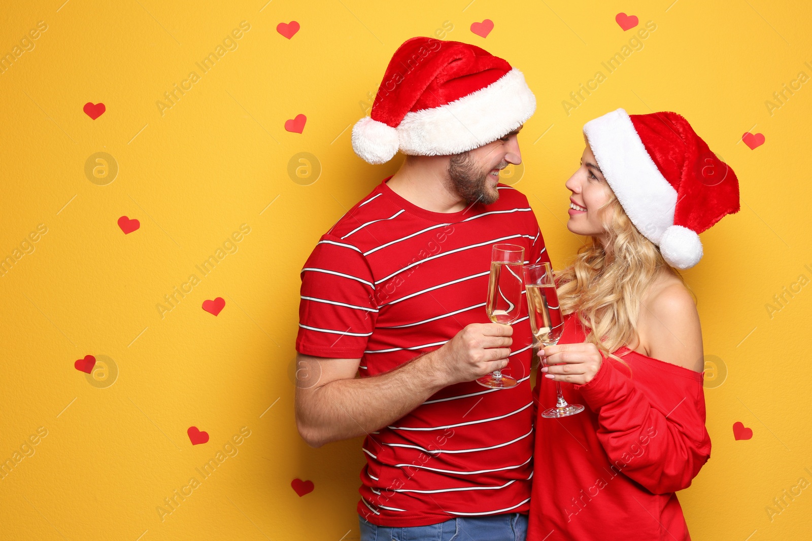 Photo of Young couple in Santa hats with glasses of champagne on color background. Christmas celebration