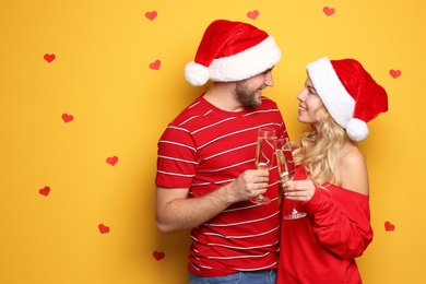 Young couple in Santa hats with glasses of champagne on color background. Christmas celebration