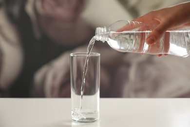 Photo of Woman pouring water from bottle into glass on table against blurred background, closeup