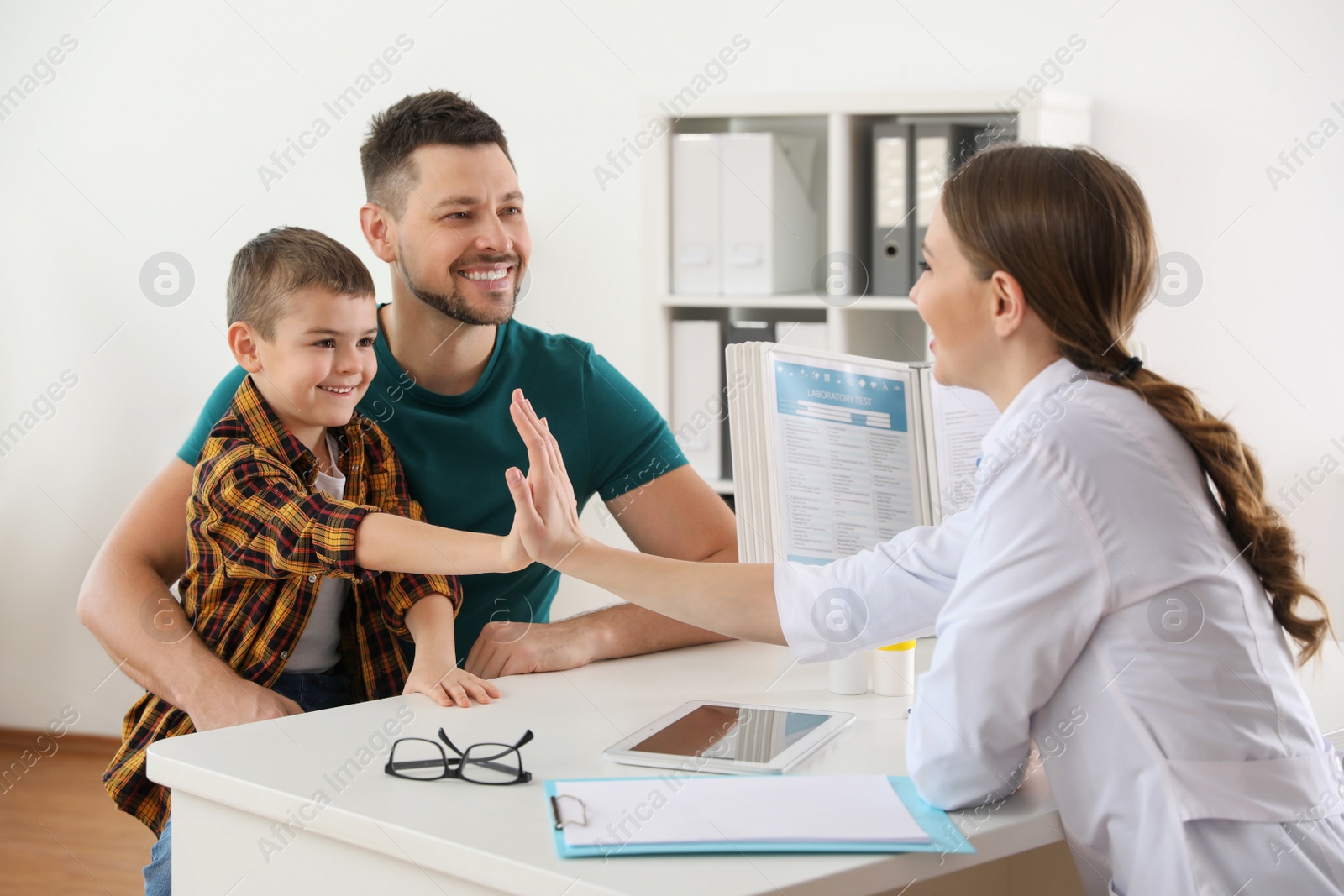 Photo of Father and son visiting pediatrician. Doctor working with little patient in hospital