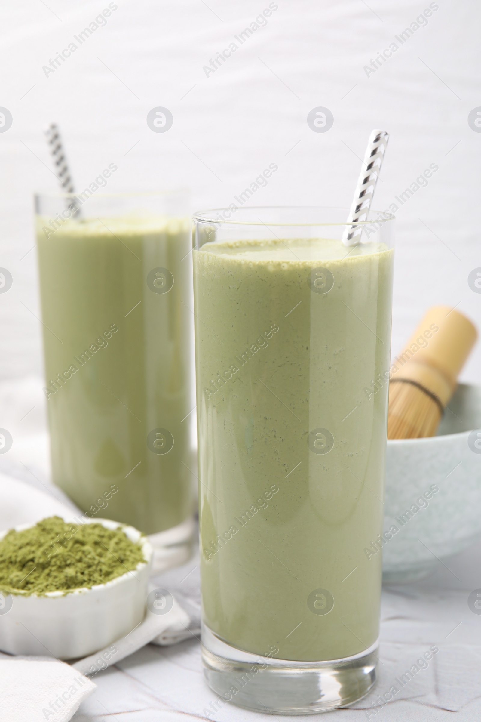 Photo of Glasses of tasty matcha smoothie and powder on white table