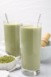 Glasses of tasty matcha smoothie and powder on white table