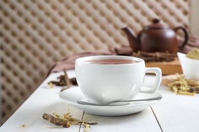 Photo of Aromatic licorice tea in cup and dried sticks of licorice root on white wooden table. Space for text