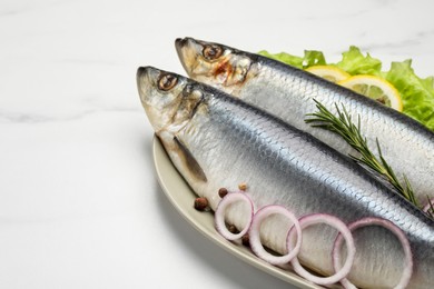 Plate with salted herrings, onion rings, slices of lemon, peppercorns and lettuce on white marble table, closeup