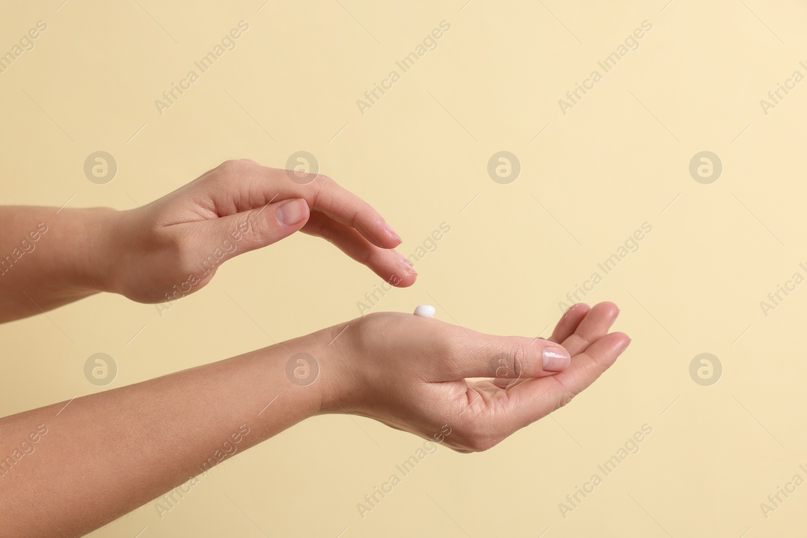 Photo of Woman applying cosmetic cream onto hand on beige background, closeup