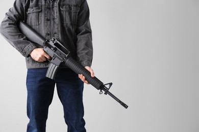 Photo of Assault gun. Man holding rifle on light background, closeup. space for text