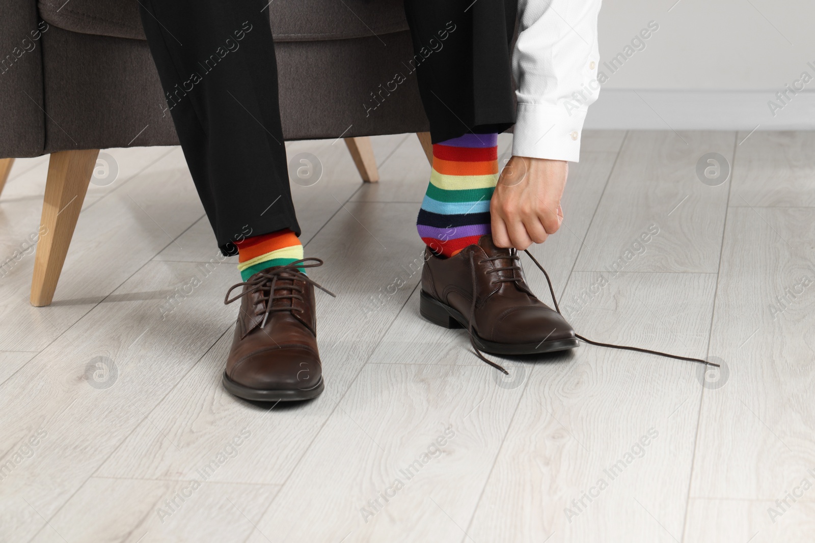 Photo of Man with colorful socks putting on stylish shoes indoors, closeup