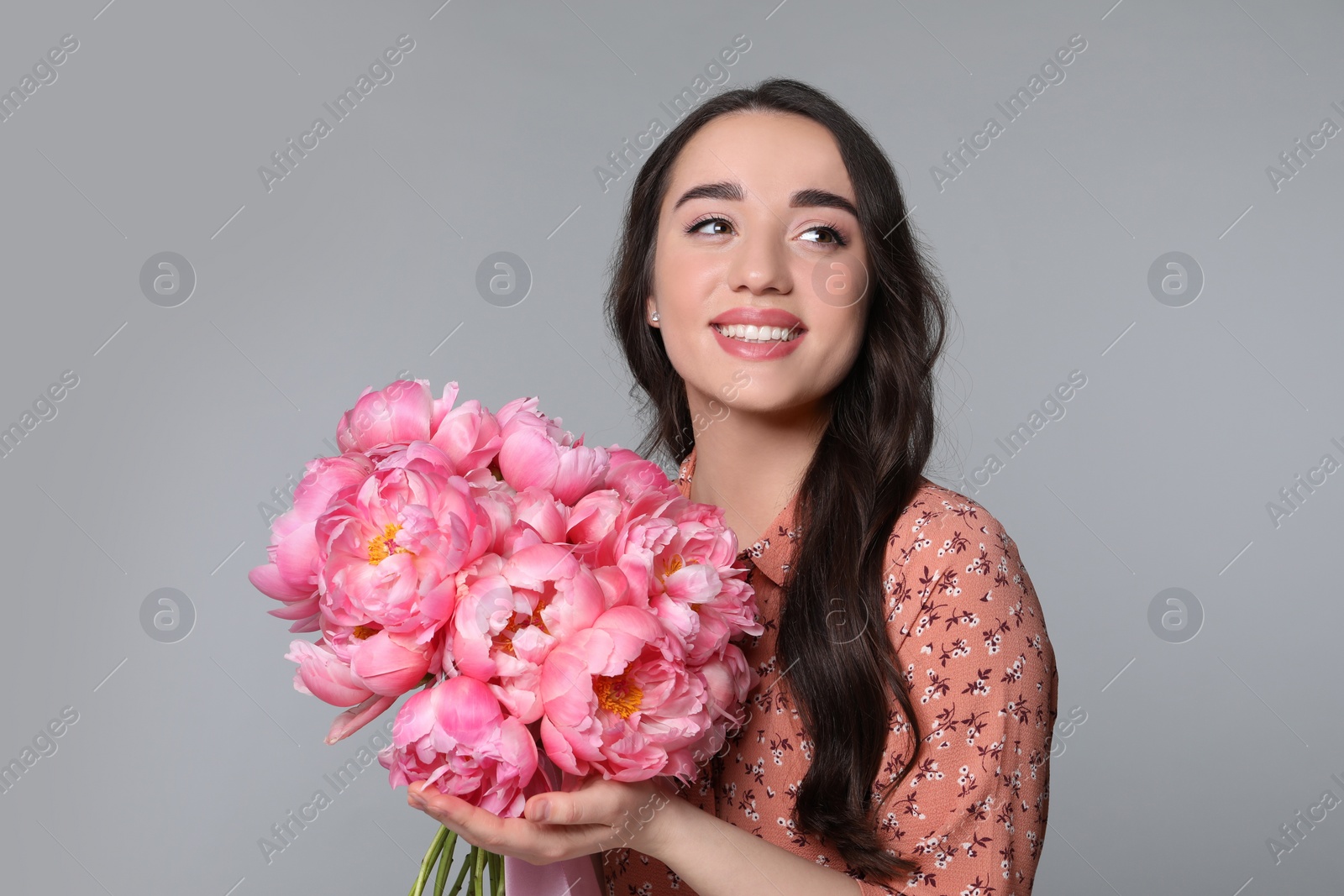 Photo of Beautiful young woman with bouquet of peonies on light grey background