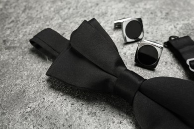 Photo of Stylish black bow tie and cufflinks on grey stone background, closeup