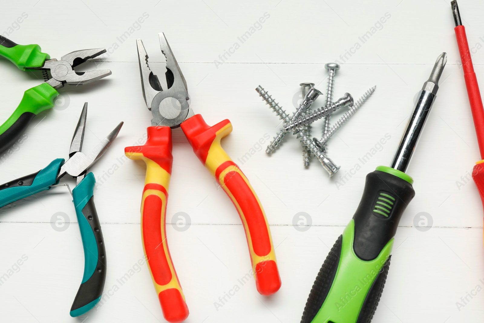 Photo of Pliers, screwdrivers and screws on white wooden table, flat lay