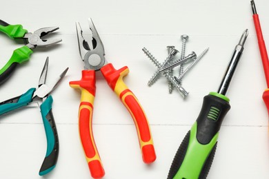 Pliers, screwdrivers and screws on white wooden table, flat lay