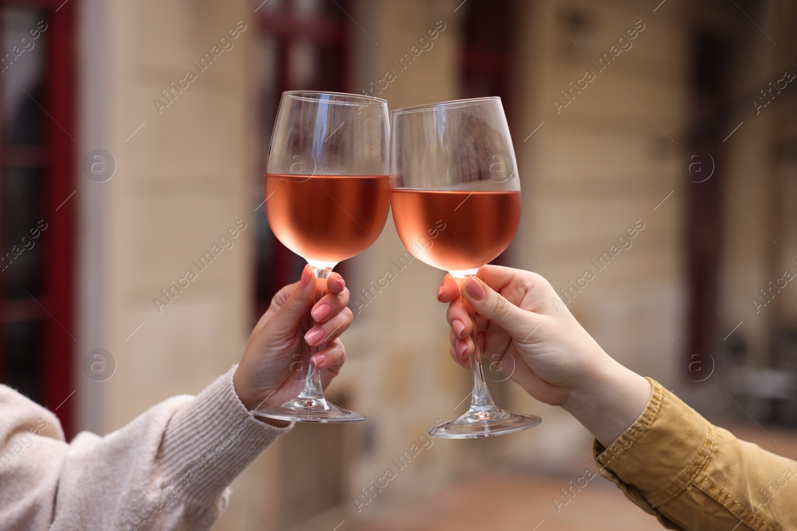 Photo of Women clinking glasses with rose wine outdoors, closeup