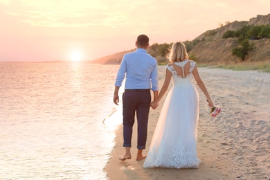 Photo of Wedding couple. Bride and groom walking at sunset on beach