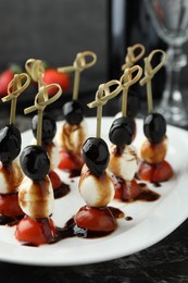 Photo of Tasty canapes with black olives, mozzarella and cherry tomatoes on dark textured table, closeup