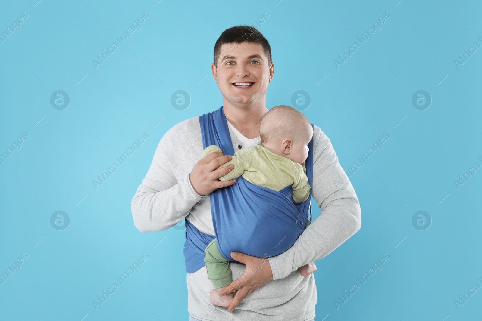 Photo of Father holding his child in sling (baby carrier) on light blue background