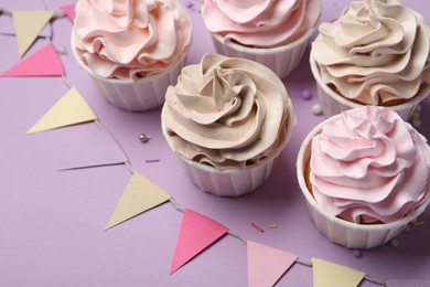 Photo of Delicious birthday cupcakes, sprinkles and bunting flags on violet background, closeup