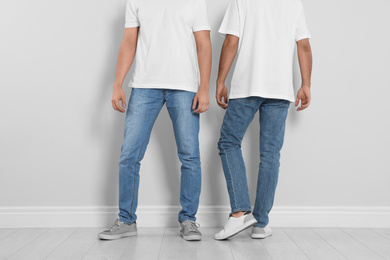 Young men in stylish jeans near light wall, closeup