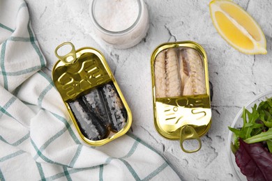 Photo of Open tin cans with mackerel fillets and spices on light textured background, flat lay