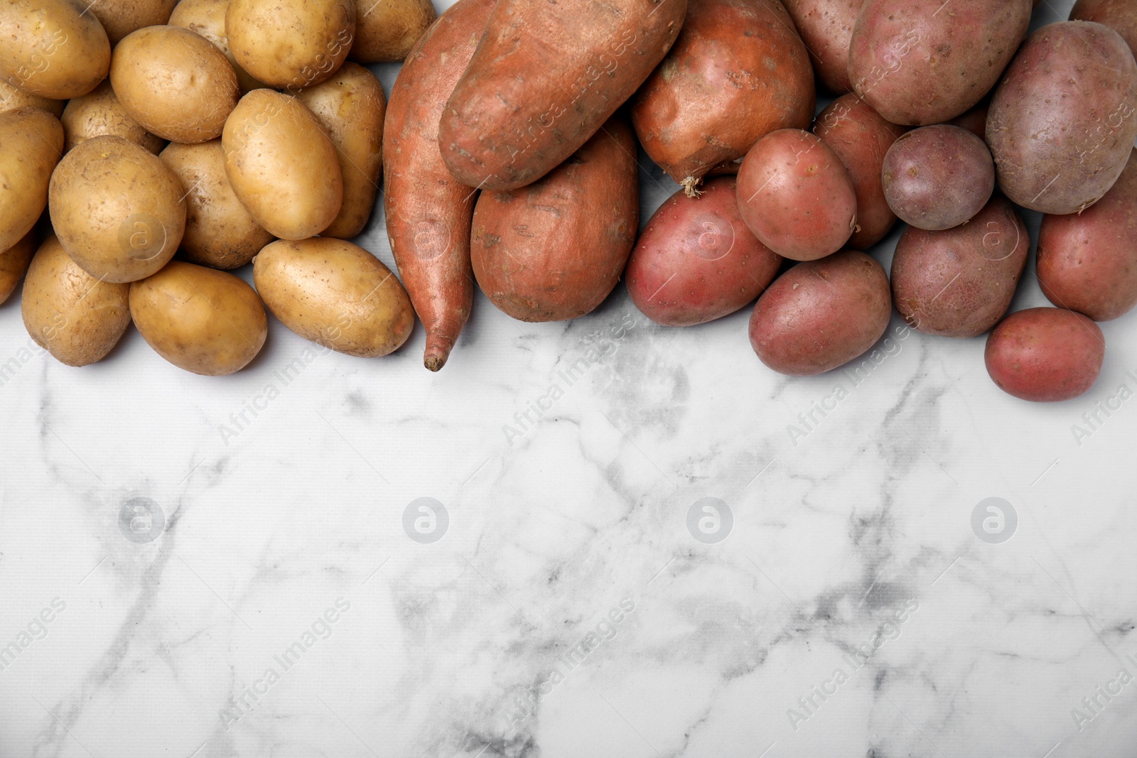 Photo of Different types of fresh potatoes on white marble table, flat lay. Space for text