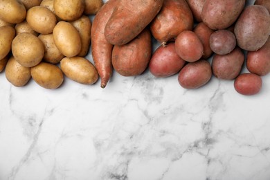Photo of Different types of fresh potatoes on white marble table, flat lay. Space for text
