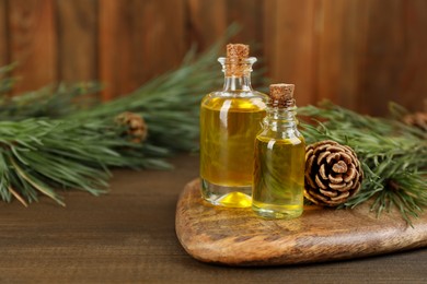 Photo of Pine essential oil, cone and branches on wooden table. Space for text