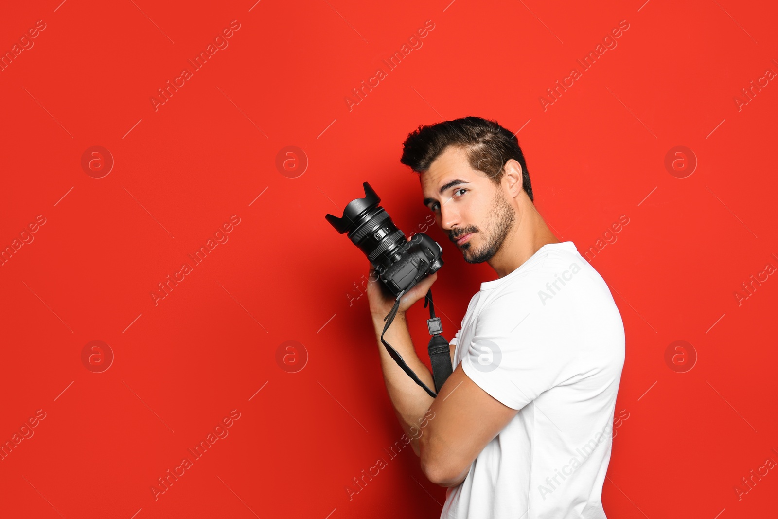 Photo of Young photographer with professional camera on red background. Space for text