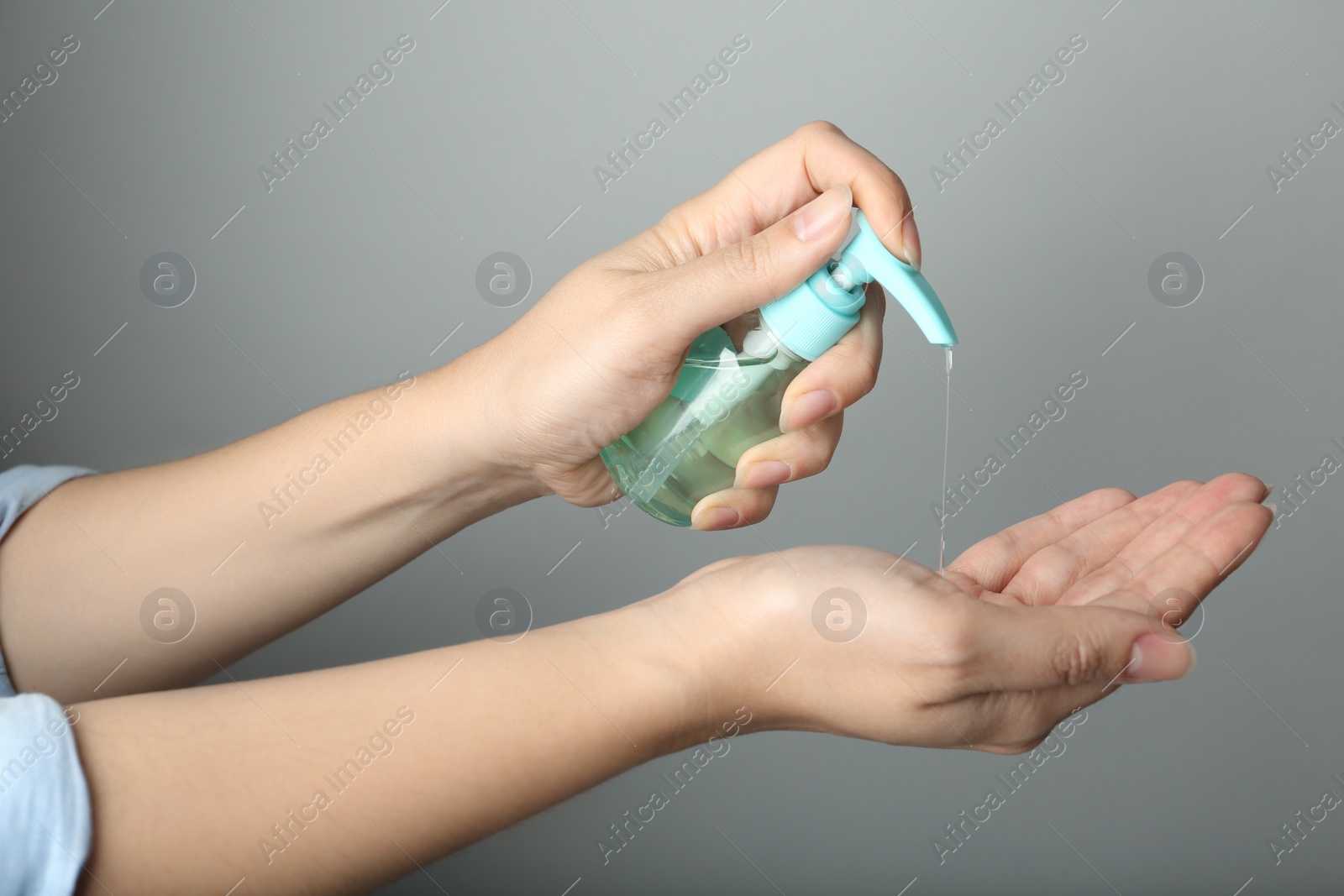 Photo of Woman applying antiseptic gel onto hand against light grey background, closeup. Virus prevention