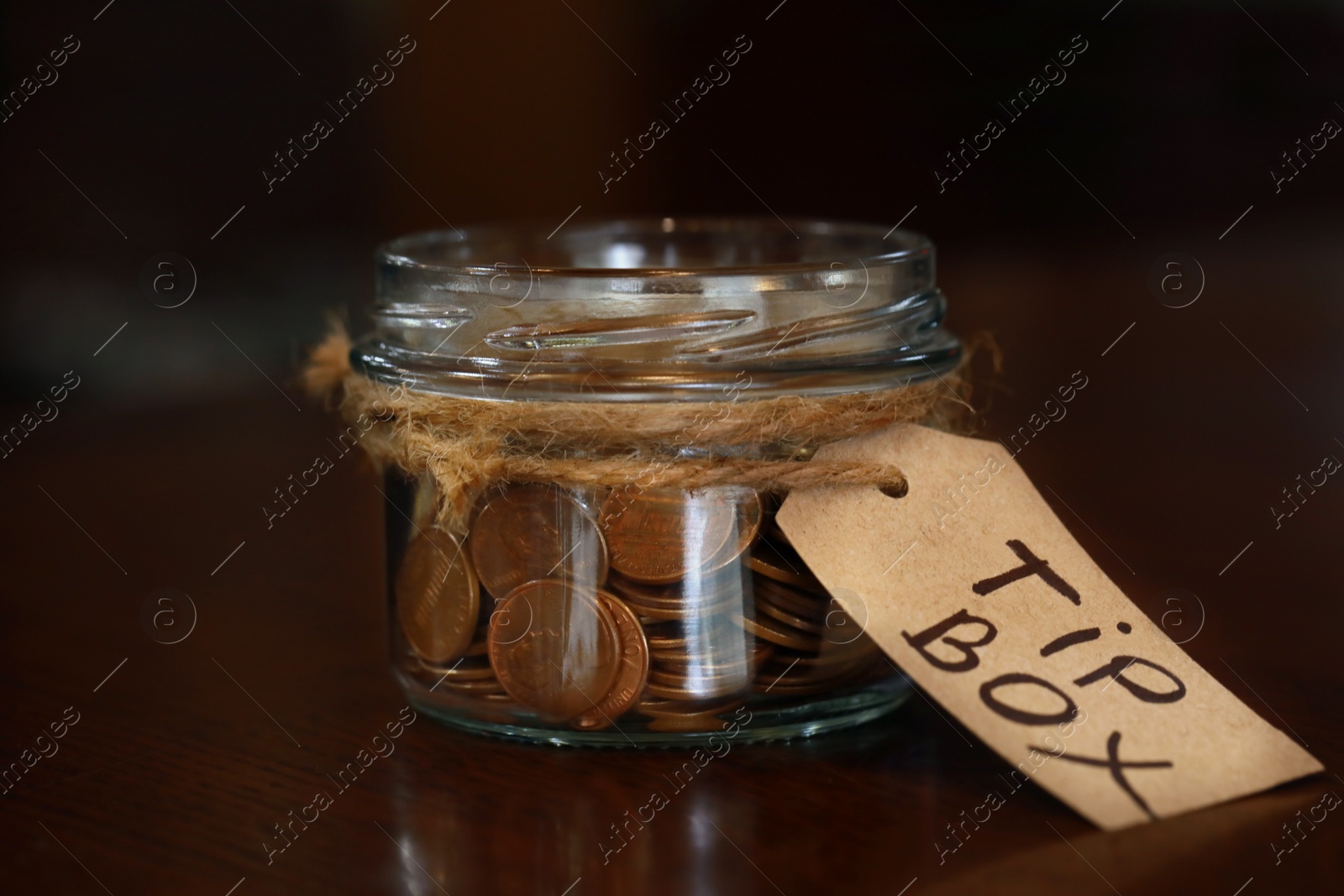 Photo of Tip box full of coins on wooden table in cafe, closeup