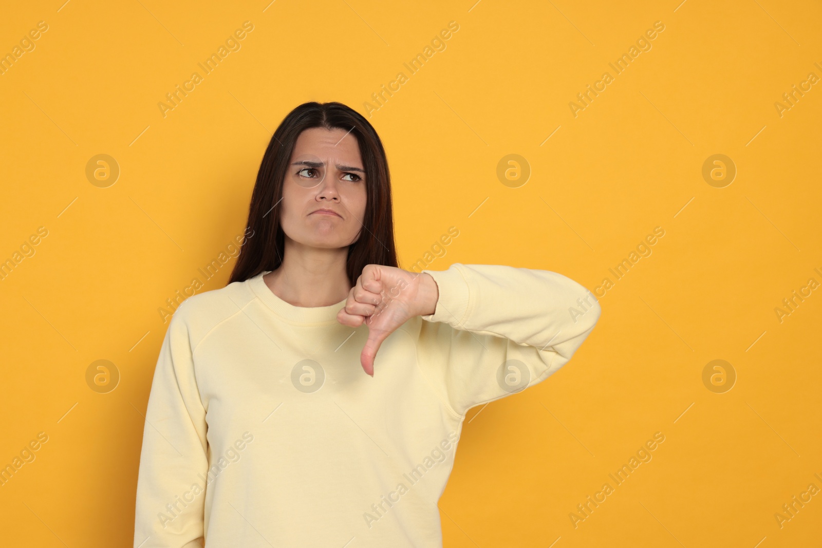 Photo of Young woman showing thumb down on orange background