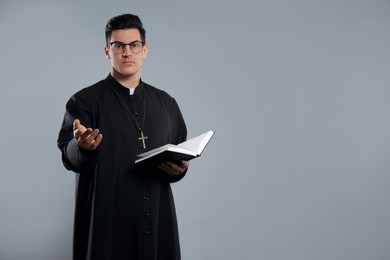 Photo of Priest with Bible on grey background. Space for text