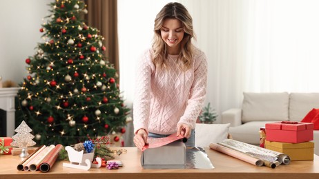 Photo of Beautiful young woman wrapping Christmas gift at home