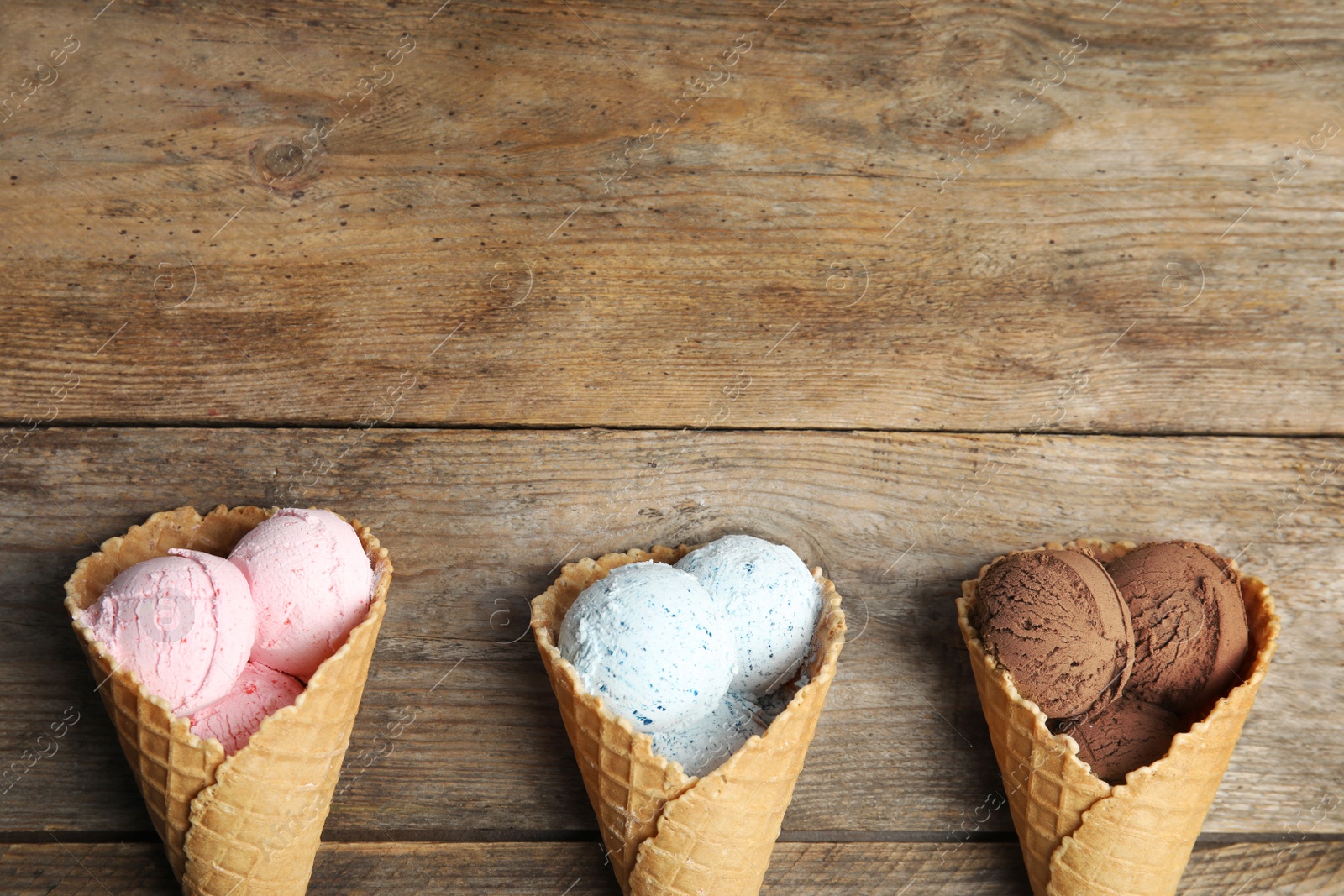 Photo of Flat lay composition with delicious ice creams in waffle cones on wooden table, space for text