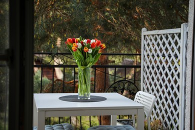 Photo of Beautiful colorful tulips in glass vase on white table at balcony