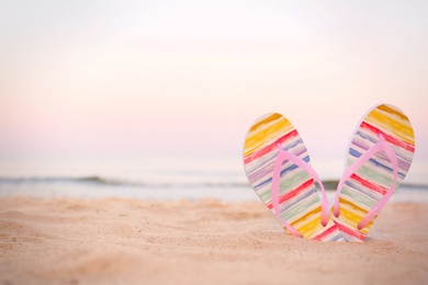 Photo of Stylish flip flops on sand near sea, space for text. Beach accessories