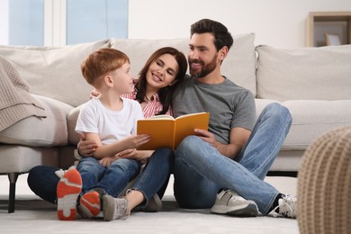 Happy parents with their child reading book on floor at home