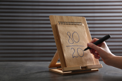 Photo of Woman writing 80/20 rule representation in notebook at grey table, closeup. Pareto principle concept