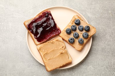 Photo of Tasty peanut butter sandwiches with jam and fresh blueberries on gray table, top view