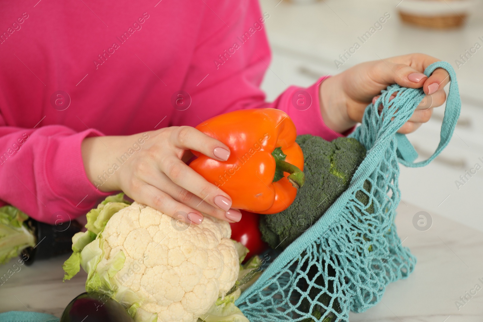 Photo of Woman taking pepper out from string bag at light marble table, closeup