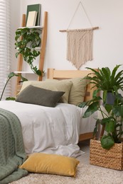 Large comfortable bed and potted houseplants in stylish bedroom. Interior design