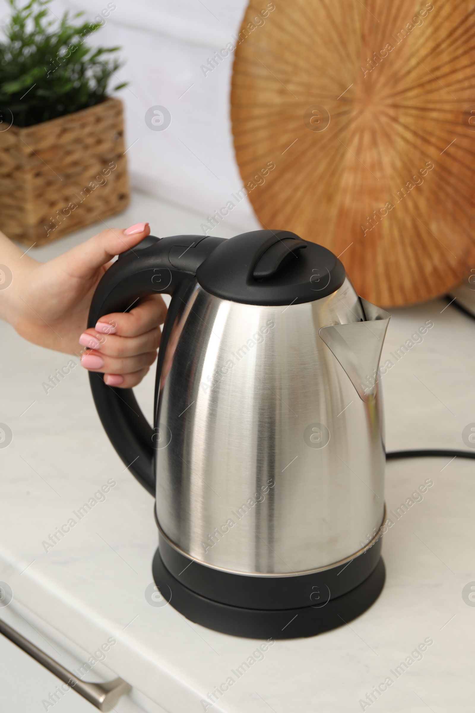 Photo of Woman with electric kettle in kitchen, closeup