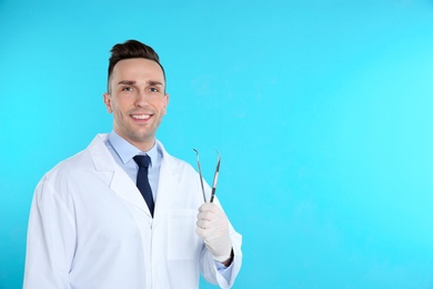 Male dentist holding professional tools on color background. Space for text