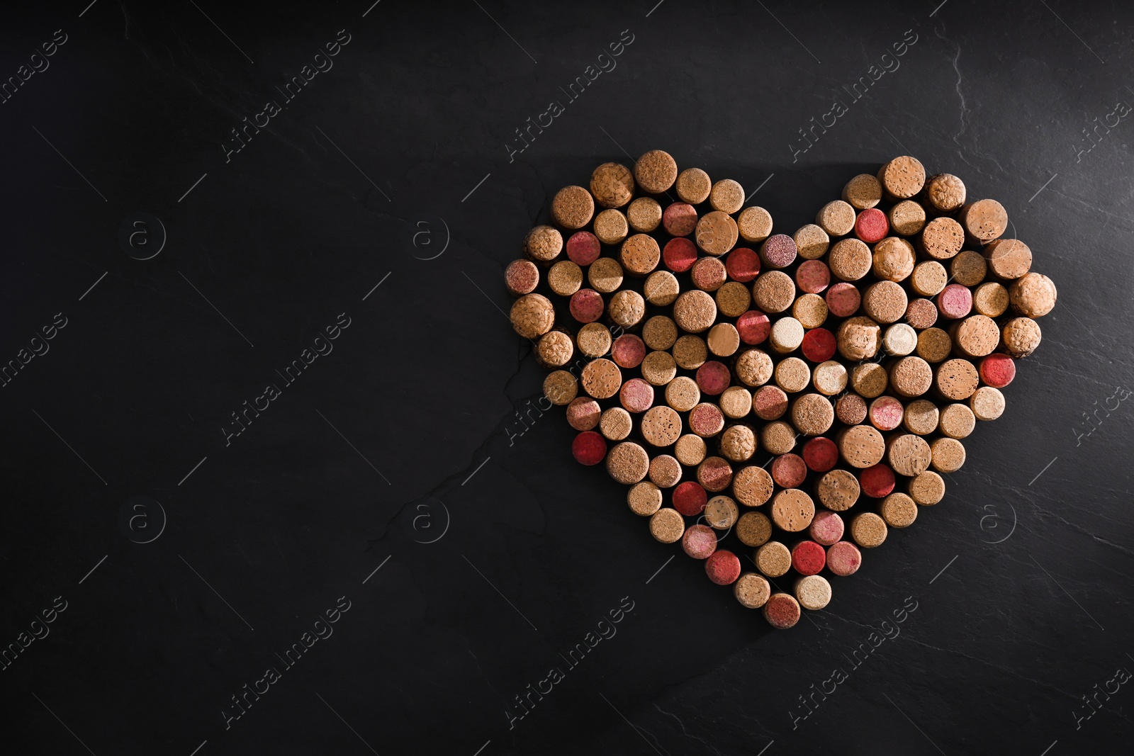 Photo of Heart made of wine bottle corks on black table, top view. Space for text