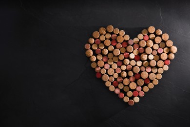 Photo of Heart made of wine bottle corks on black table, top view. Space for text