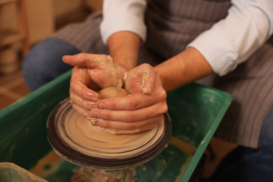 Man crafting with clay on potter's wheel indoors, closeup