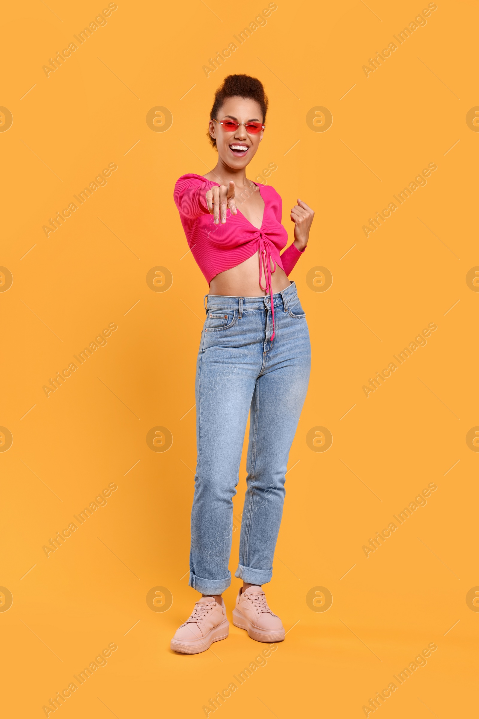 Photo of Happy young woman in stylish sunglasses dancing on orange background