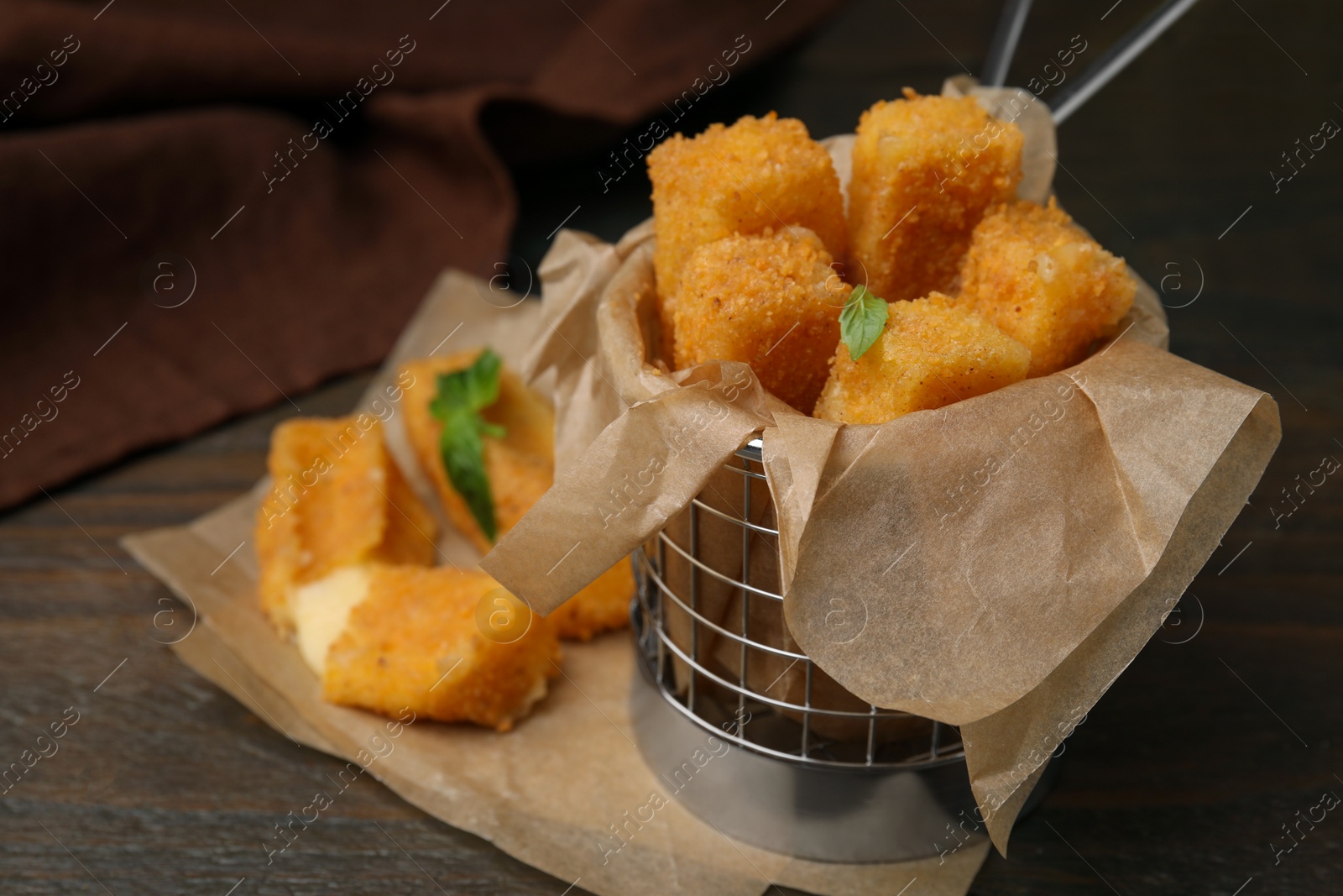 Photo of Metal basket with tasty fried mozzarella sticks on wooden table, closeup