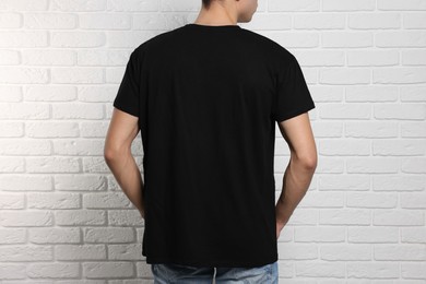 Man wearing black t-shirt near white brick wall, back view. Mockup for design