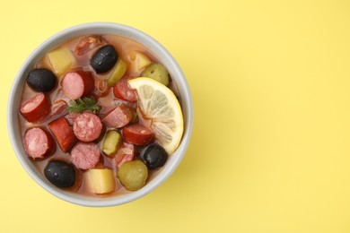 Photo of Meat solyanka soup with thin dry smoked sausages in bowl on pale yellow background, top view. Space for text