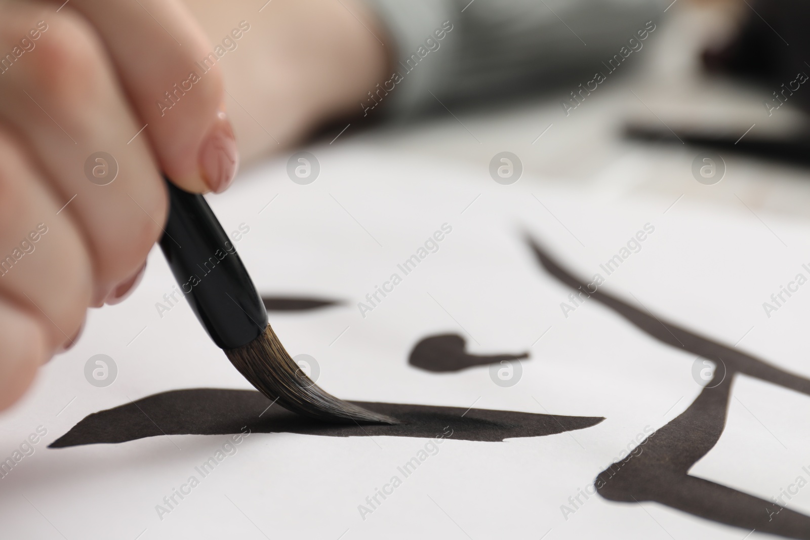 Photo of Calligraphy. Woman with brush writing hieroglyphs on paper at table, closeup